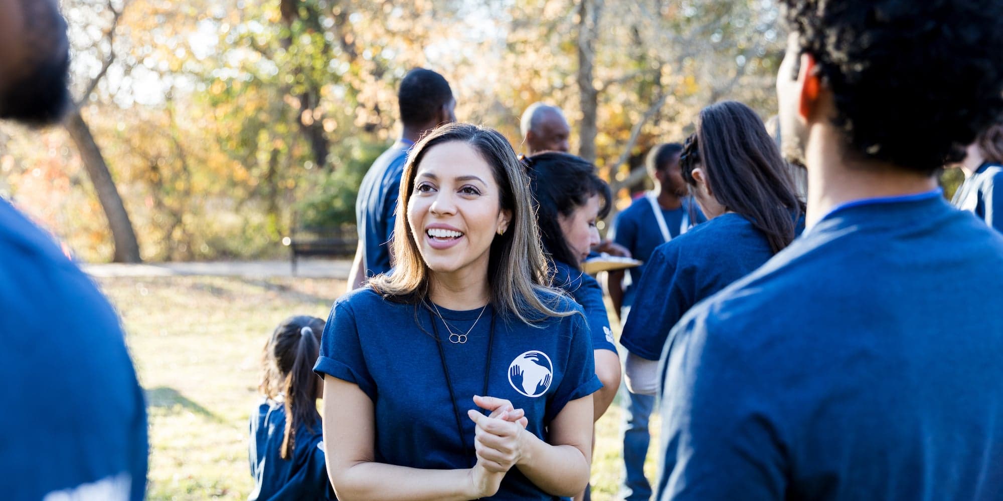person talking to two volunteer workers outside, with other volunteers in the background